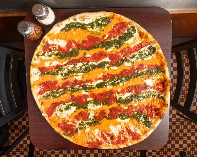 Overhead view of a large pizza with stripes of red sauce, orange vodka sauce, and green pesto.