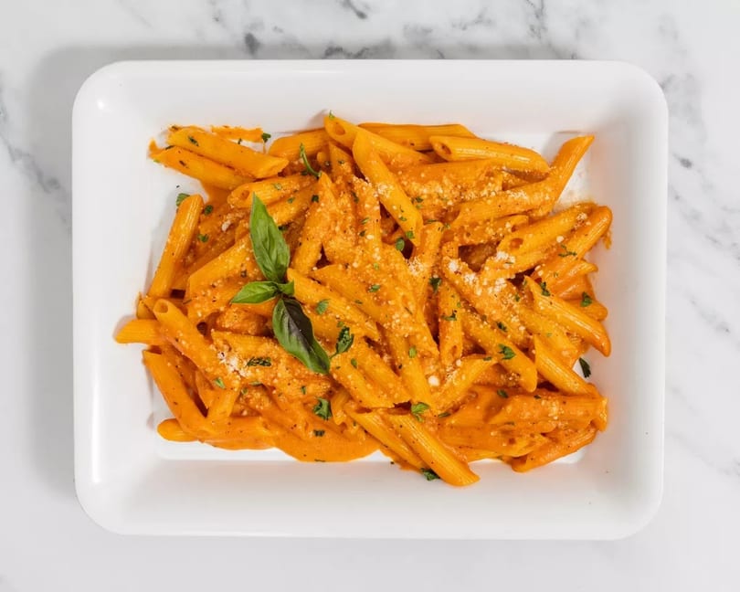 Penne pasta in a creamy orange sauce, garnished with fresh basil and grated cheese.