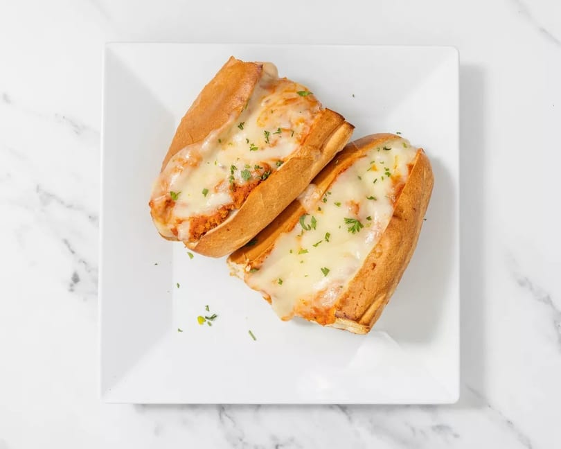 Two cheesy meatball subs on a white rectangular plate, garnished with parsley.