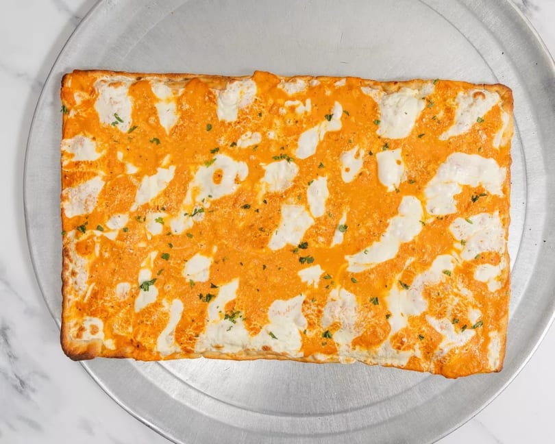 Rectangular pizza with orange sauce and white cheese swirls, garnished with herbs on a metal tray.